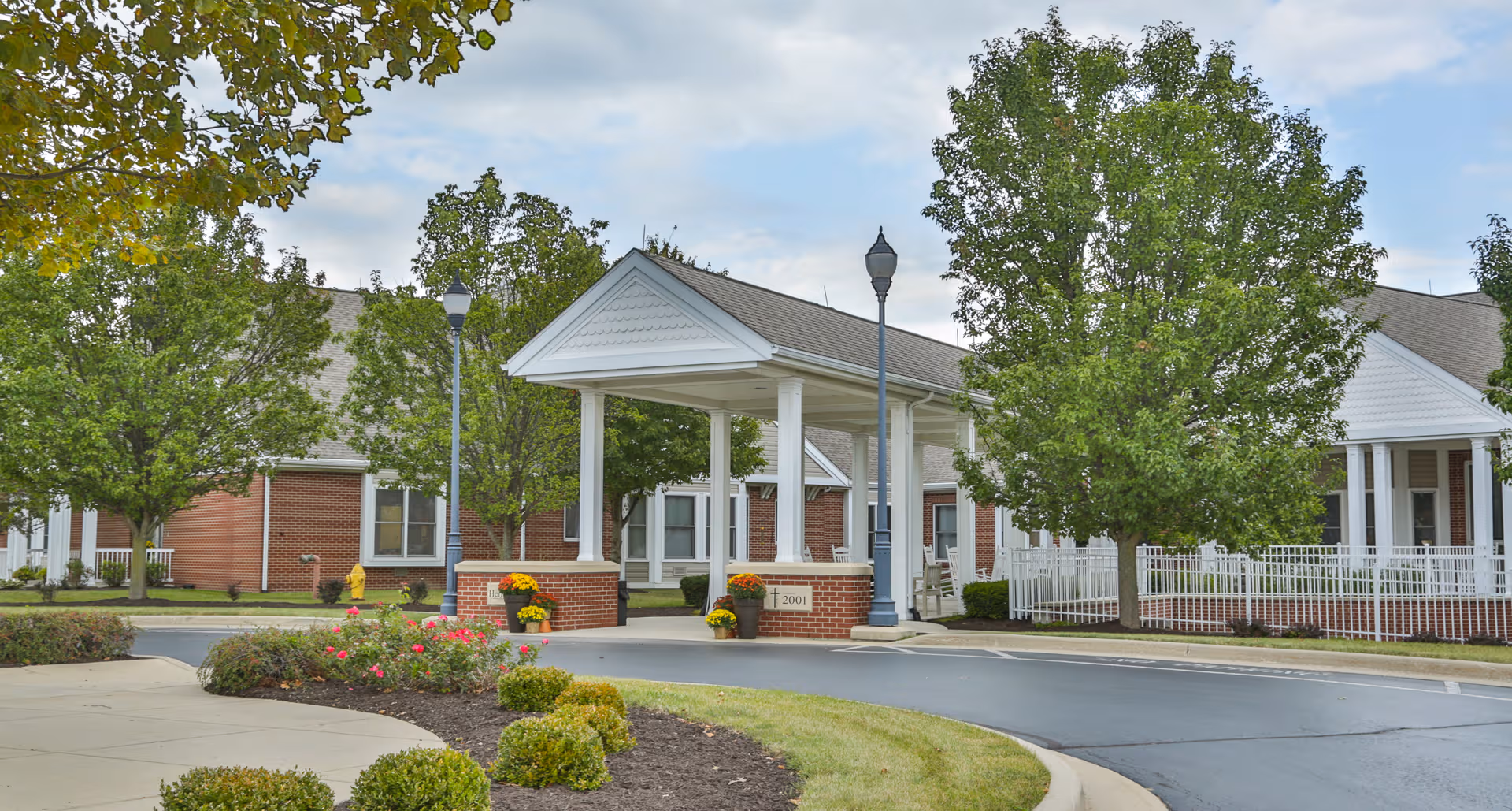 Brick senior living facility entrance with white columns, covered porch, and manicured landscaping.