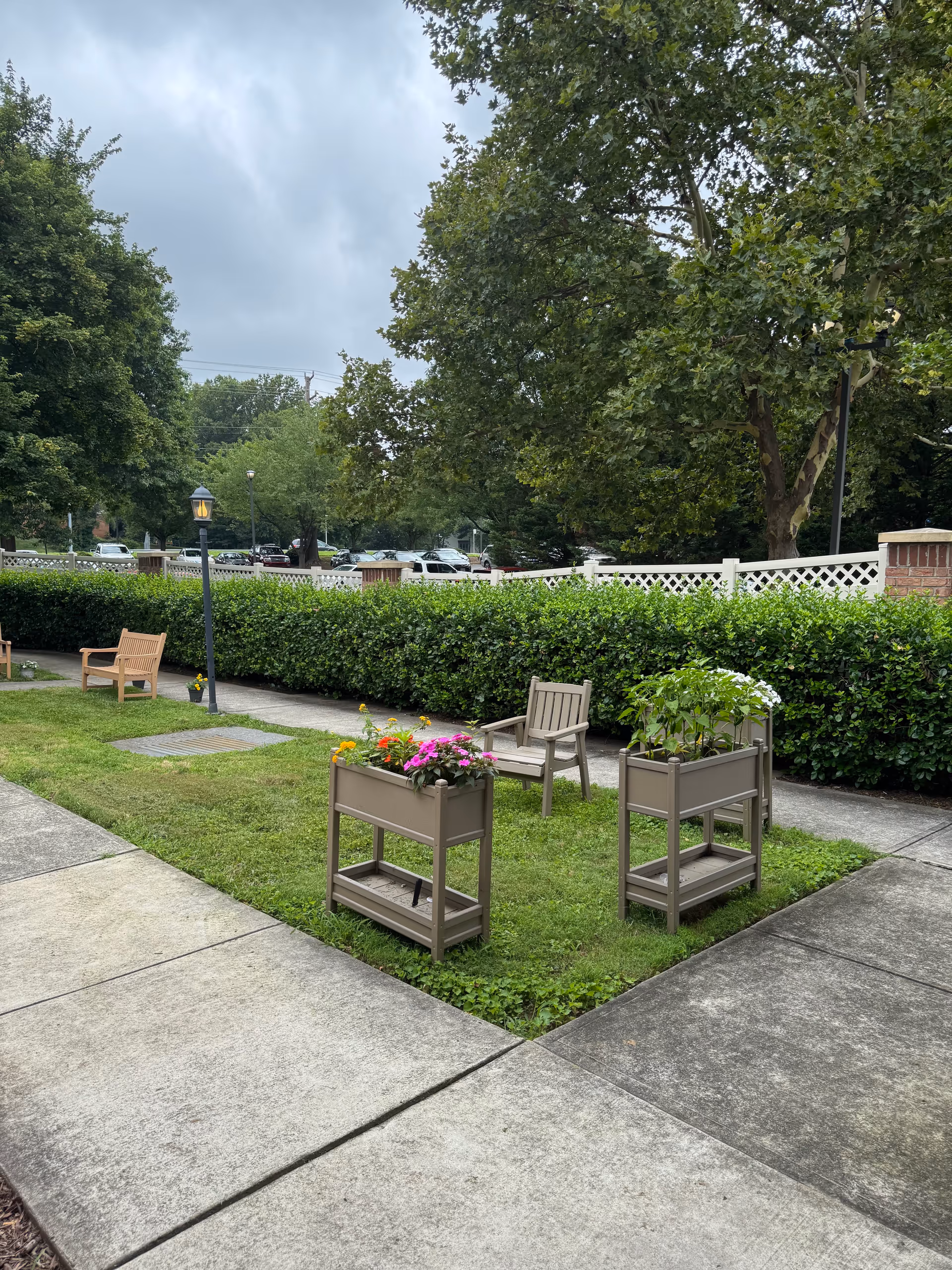 Courtyard with planters, benches, hedges, and trees beside a paved walkway.
