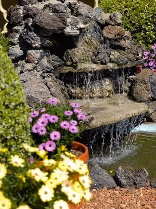 Outdoor garden fountain with cascading water over rocks and colorful flowers.