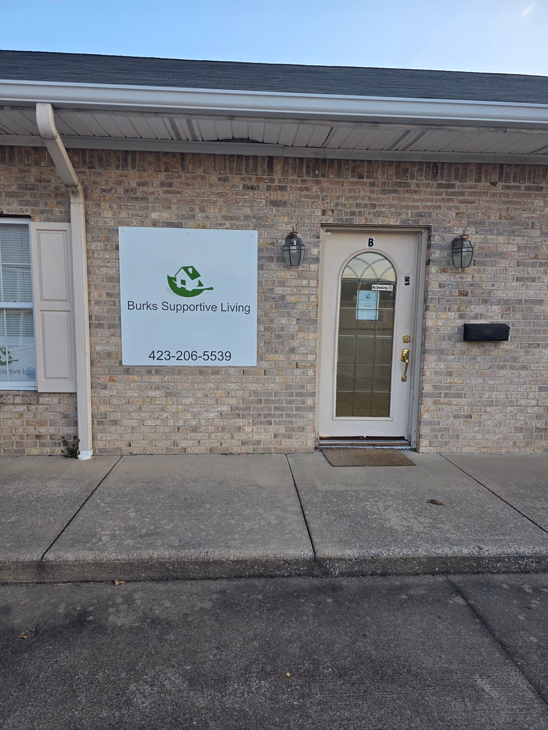 Front exterior of Burks Supportive Living with entrance door and sign on brick wall.
