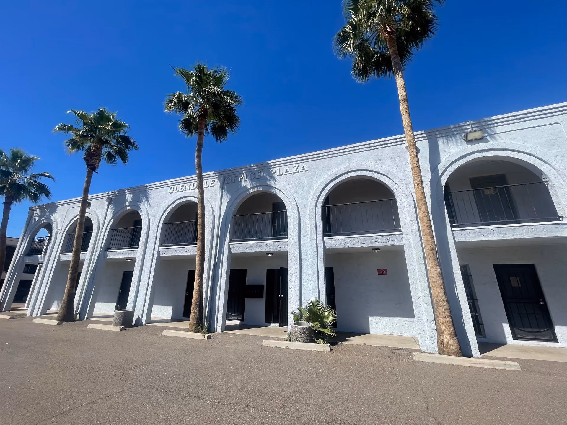 Exterior white building with arched entrances, palm trees, and a bright blue sky.