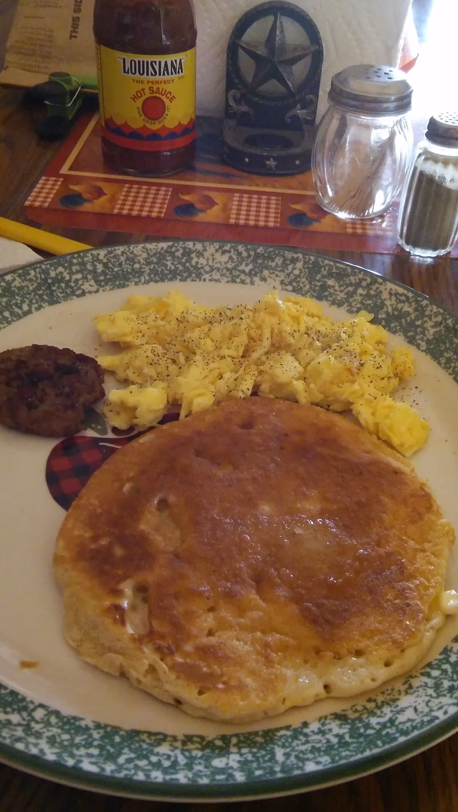 Plate with pancakes, scrambled eggs, and sausage on a dining table with condiments visible nearby.