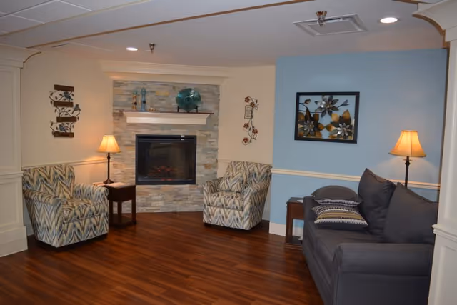 Cozy sitting area with a stone fireplace flanked by two patterned armchairs, a sofa, side tables, and lamps.
