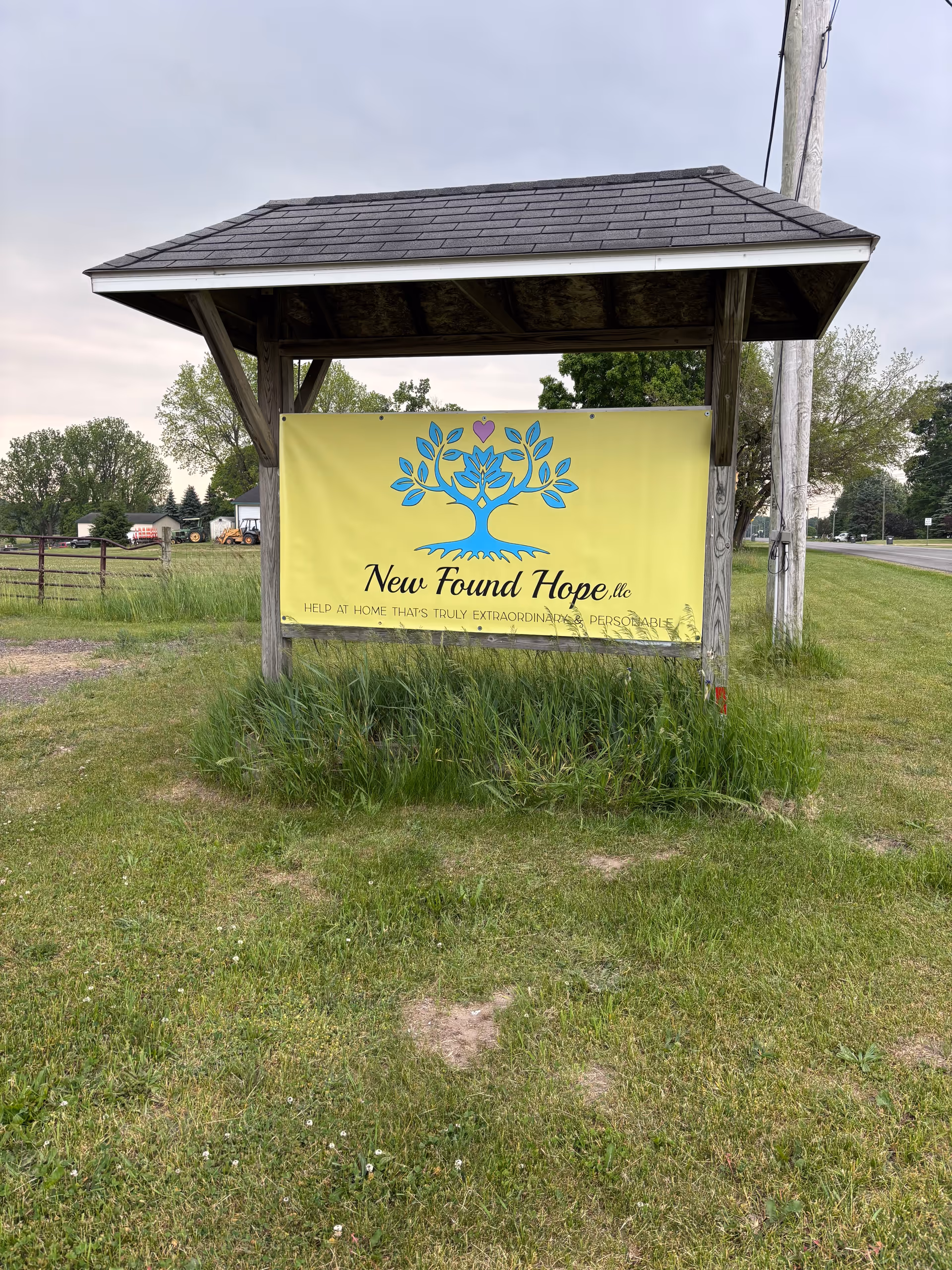 Yellow sign for New Found Hope LLC displayed under a wooden shelter beside a road.