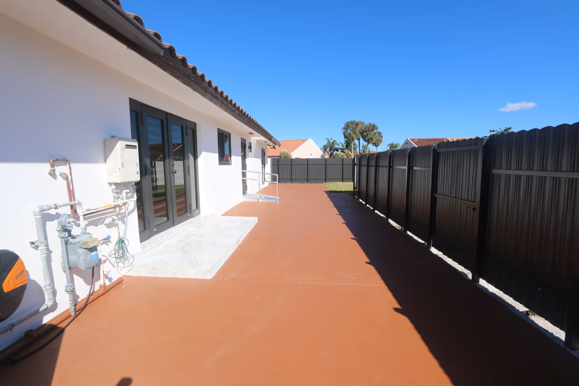 Outdoor walkway along a white senior living facility with a brown concrete path and black fence.
