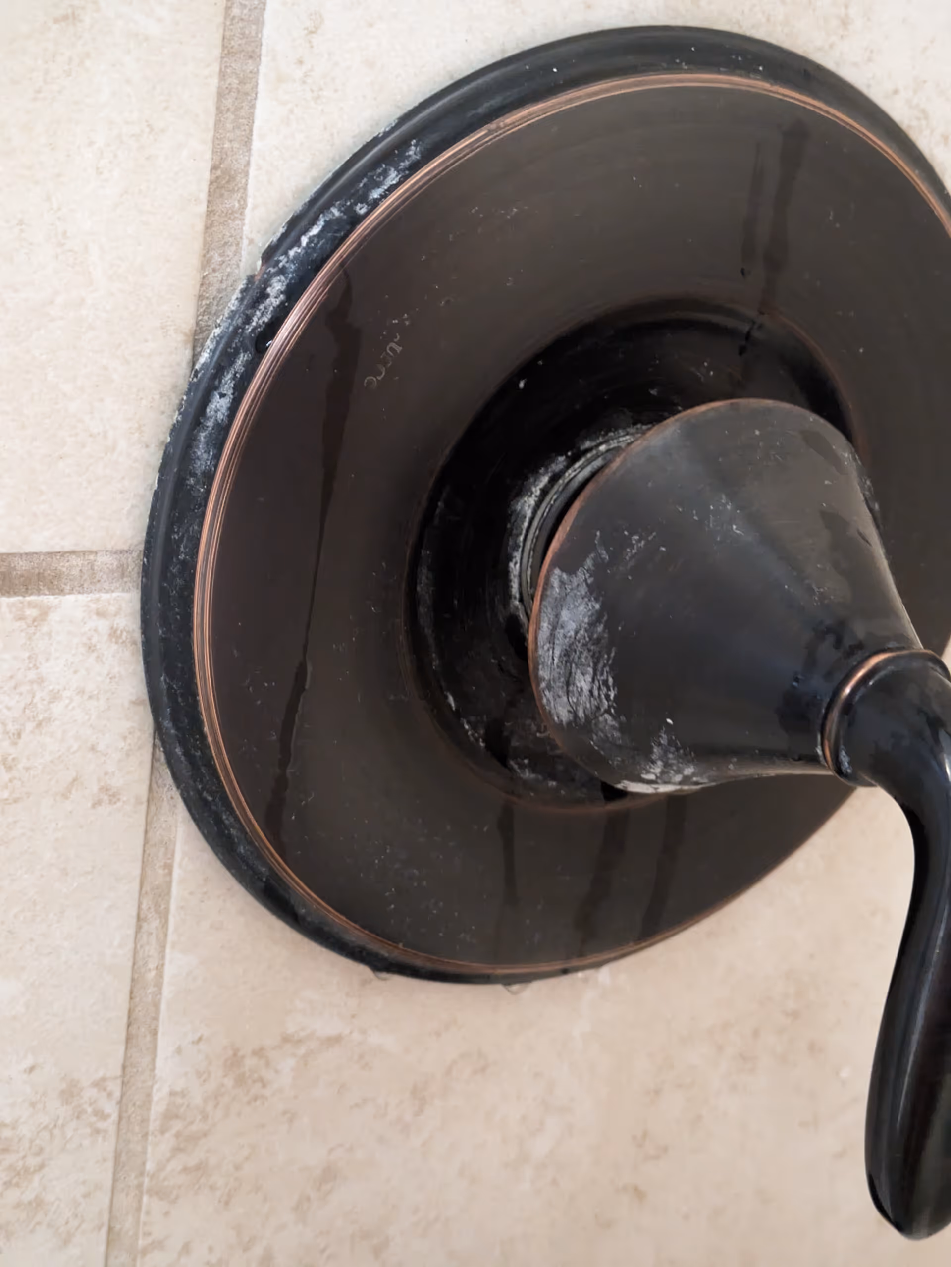 Close-up of a black bathroom faucet handle mounted on beige tiled wall.