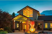 Exterior view of Panorama senior living facility at dusk with illuminated entrance and colorful sculpture.