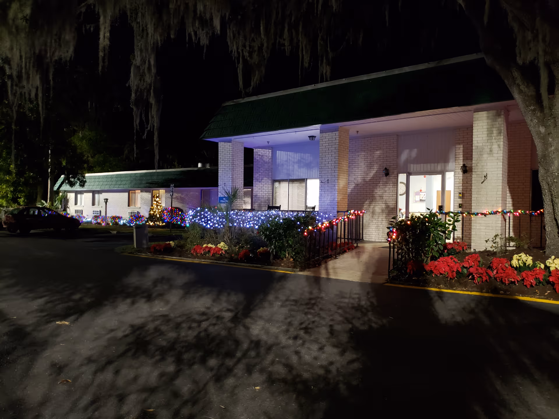 Night exterior of a facility with an illuminated entrance and holiday string lights.