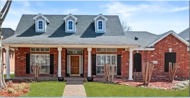 Brick senior living facility with three dormer windows, front entrance, and manicured lawn.