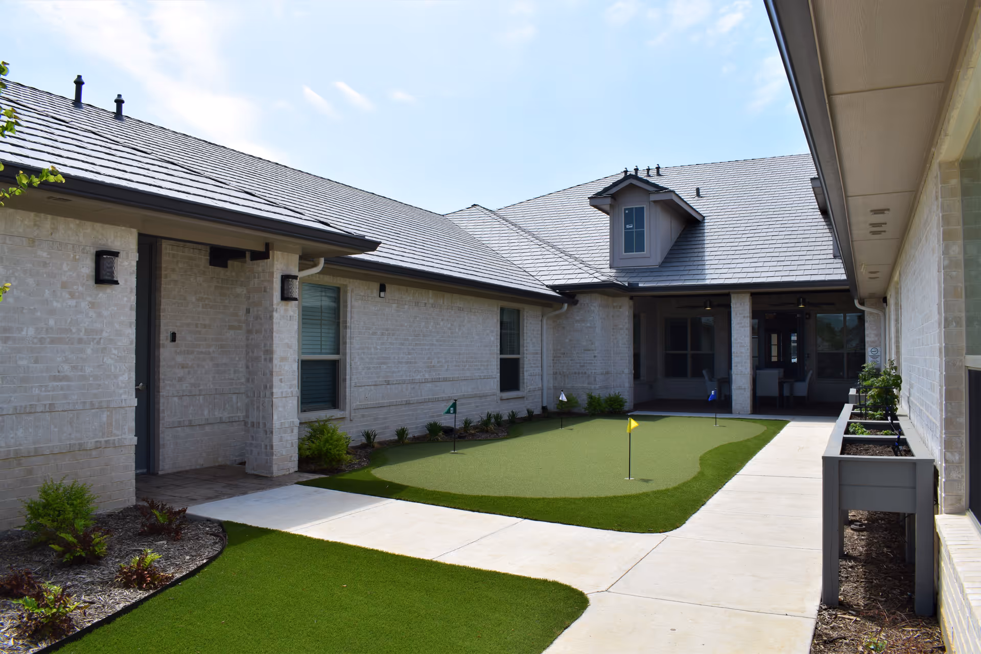 Exterior courtyard of Avalon Memory Care building with artificial turf putting area and walkways.