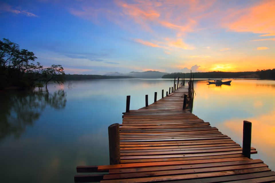 Wooden dock extends over calm lake at a colorful sunset.