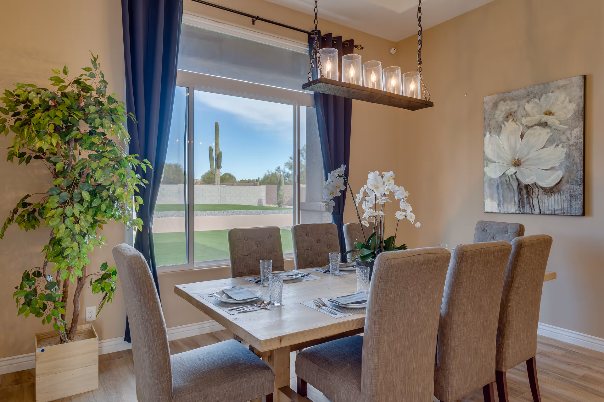 A sunlit dining room with a wooden table, upholstered chairs, and a chandelier.