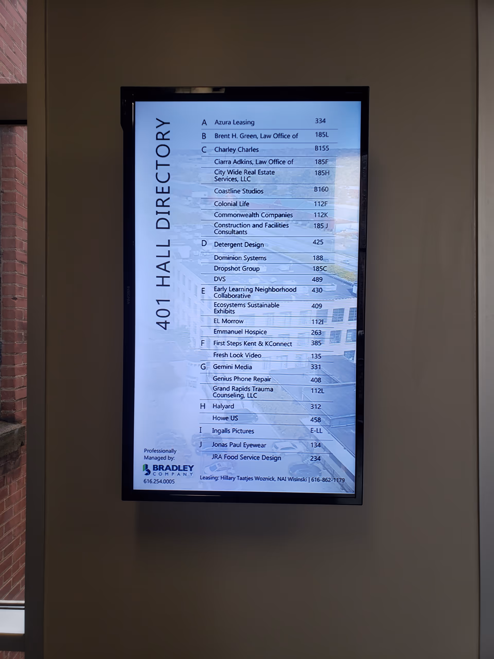 A tall digital directory sign in a hallway lists offices and numbers.