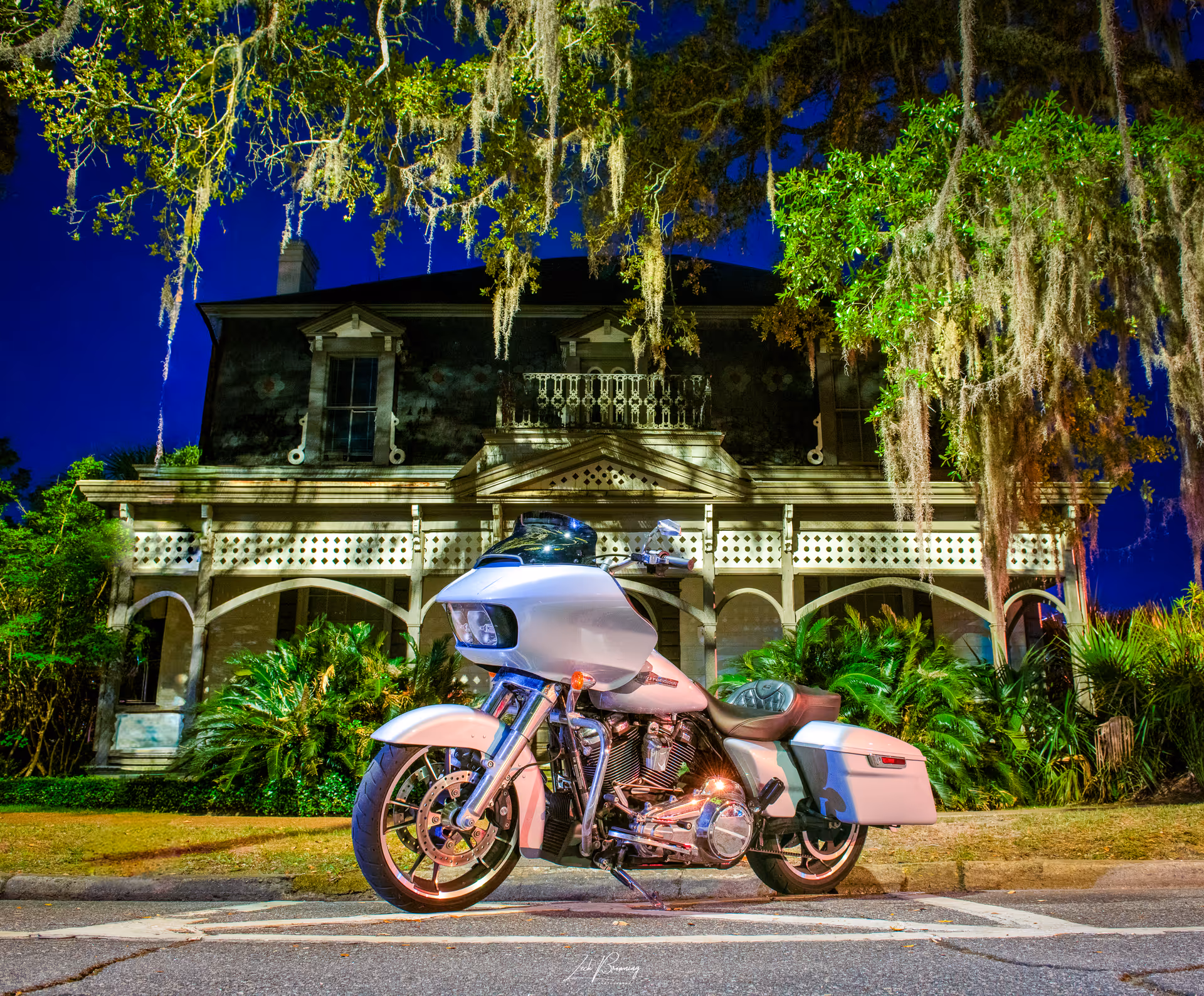 White motorcycle parked on a street in front of a large historic house.