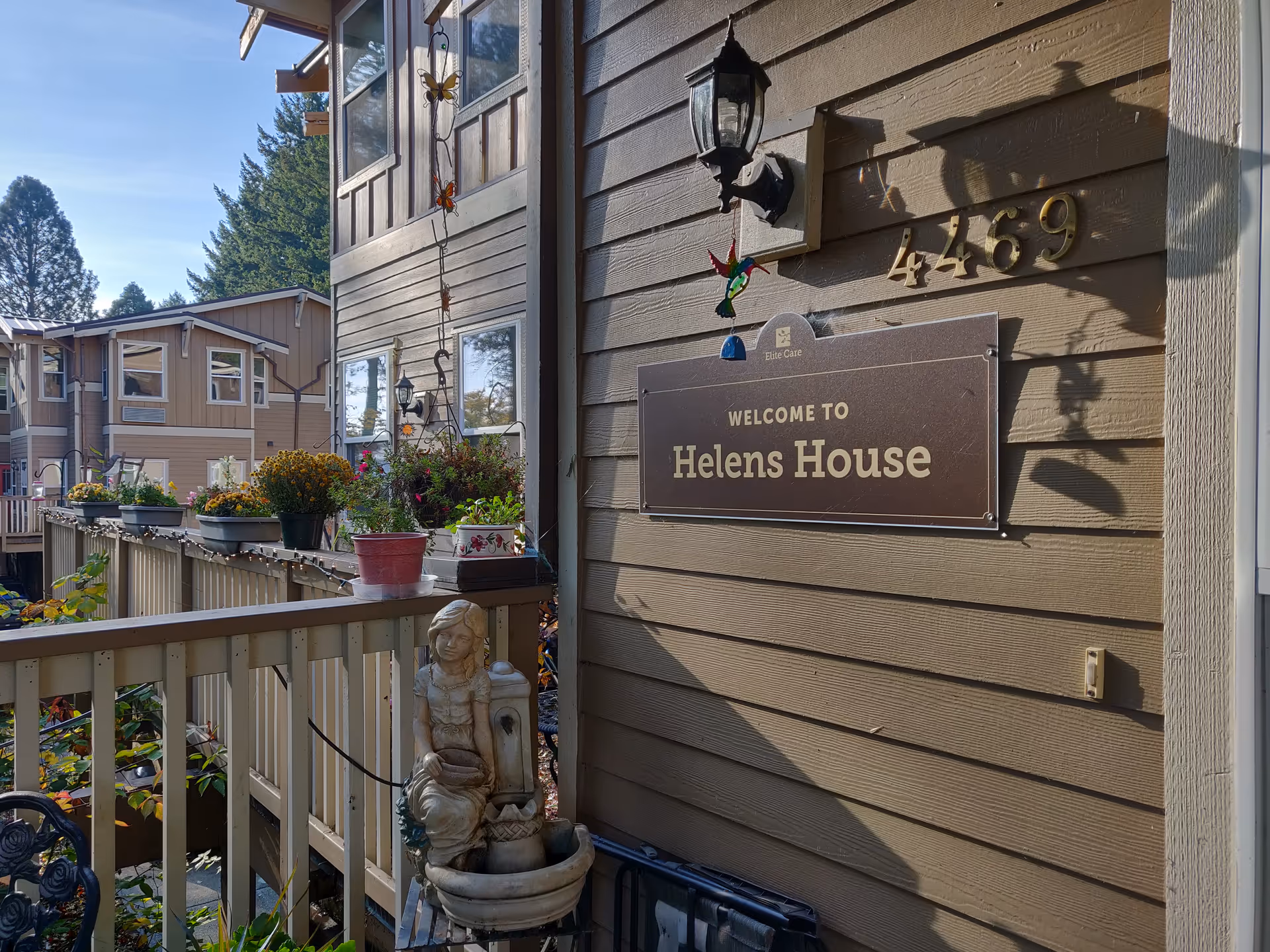 Exterior view of Helens House, a senior housing building, with a sign and potted plants.