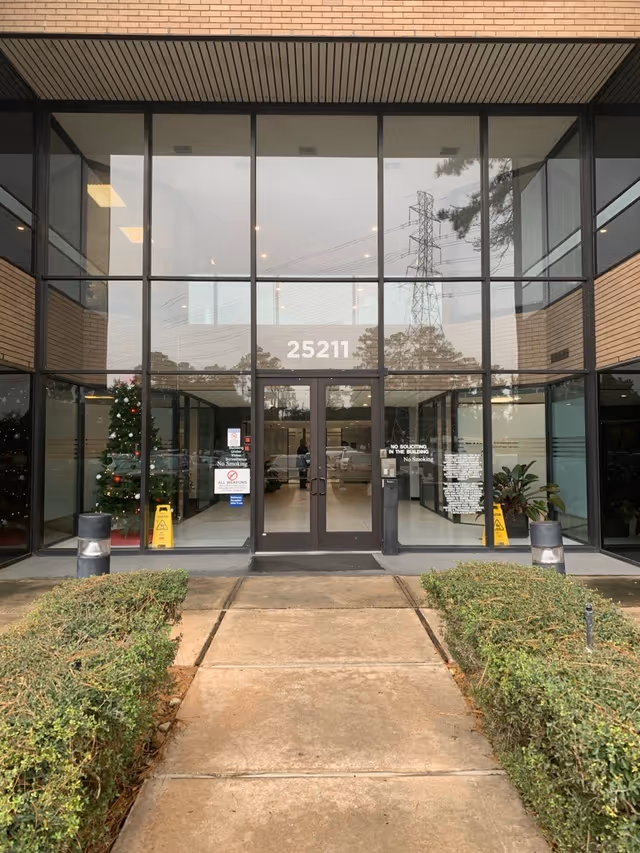 Glass-front entrance to a senior living facility with a brick exterior and walkway.