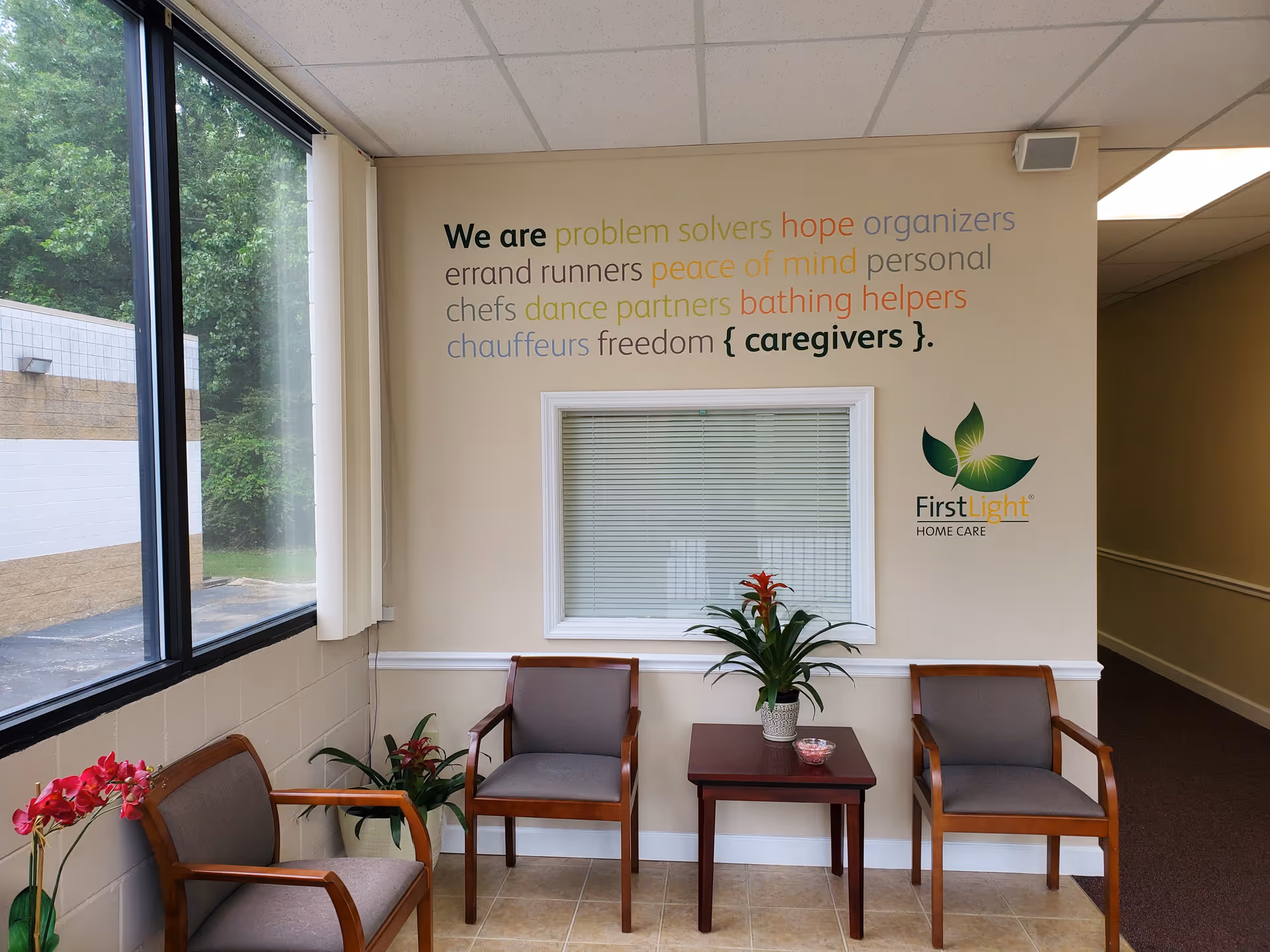 Interior waiting area with four chairs, a small table, plants, and wall text.