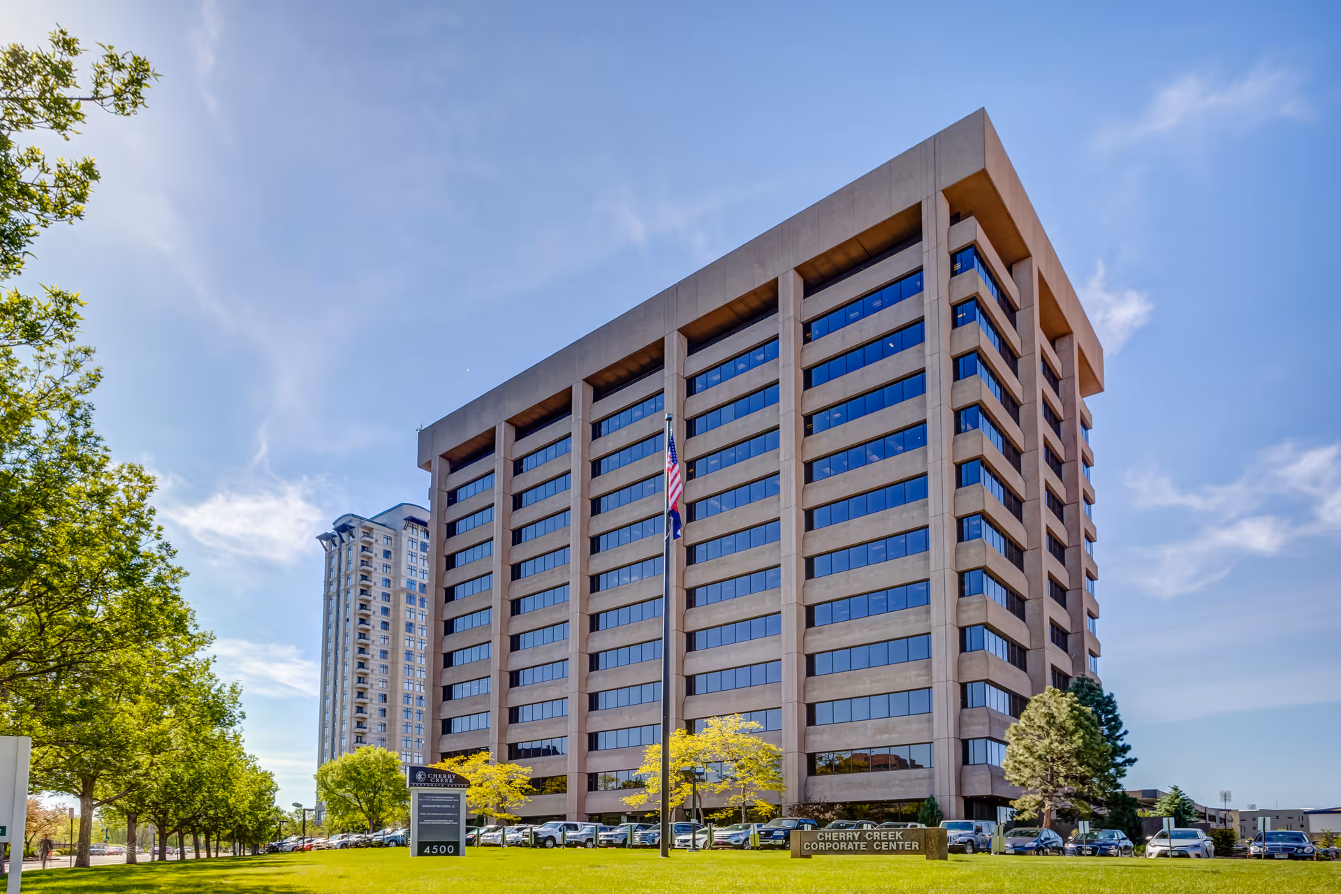 Tall modern office building with glass windows and a surrounding parking lot