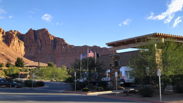 Entrance of a single-story facility with flagpoles and desert red rock cliffs in the background under a blue sky.