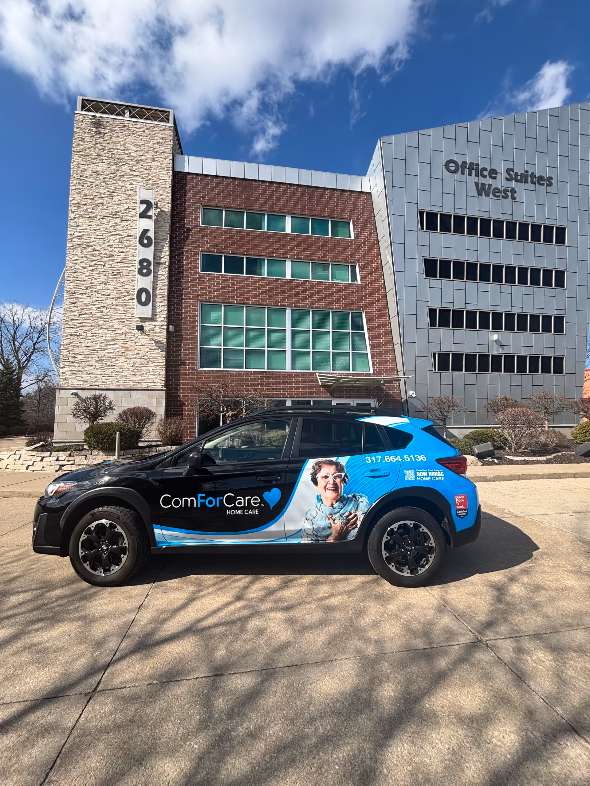 A branded ComForCare car parked in front of a modern office building labeled Office Suites West.