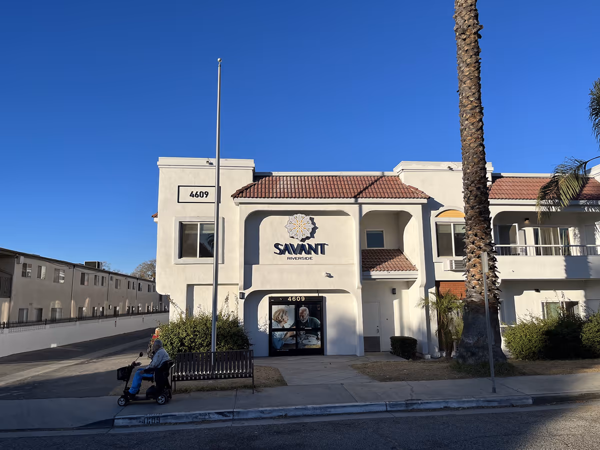 Front view of Savant of Riverside senior living building with palm trees.