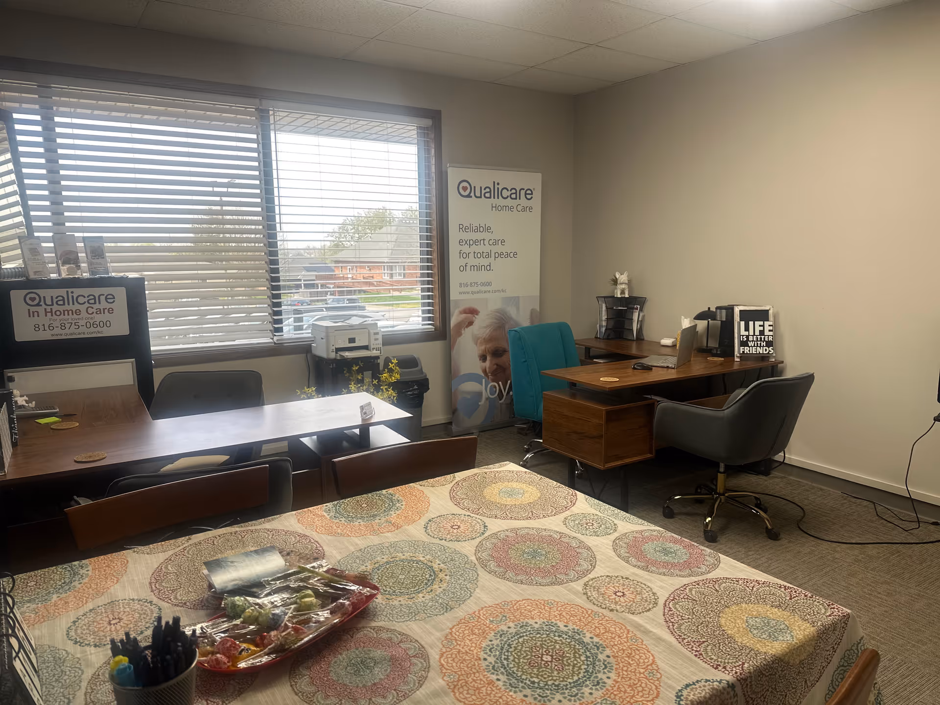 Interior office space with tables, chairs, blinds, and Qualicare signage inside a senior care facility.