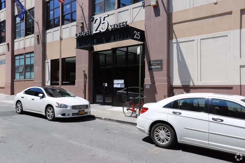 Urban building exterior with a glass entrance, parked cars, and a bicycle.