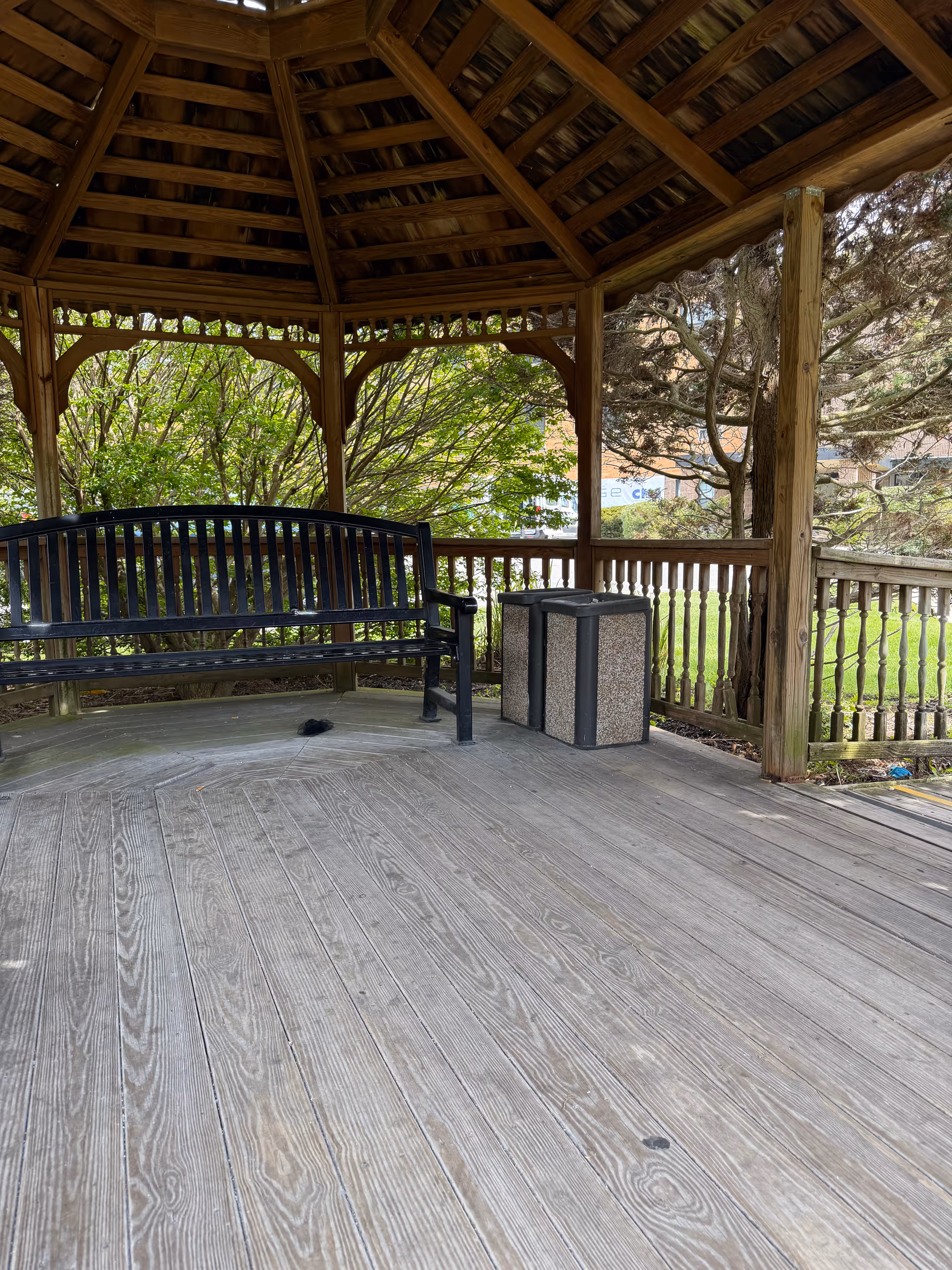 Wooden gazebo with bench and trash cans on a spacious outdoor deck.