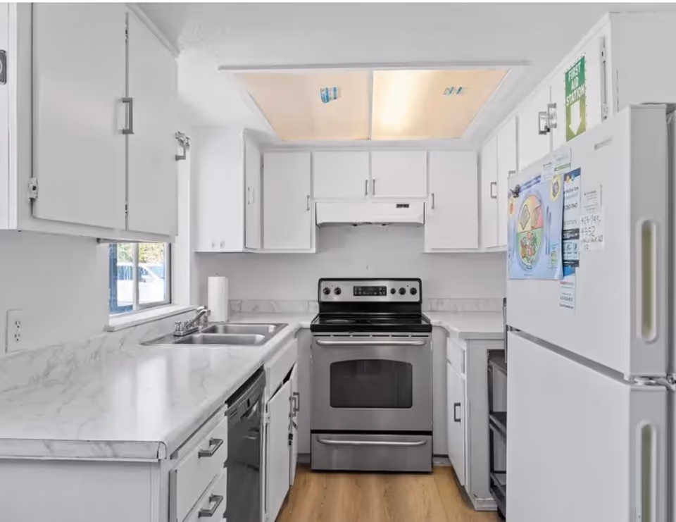 Bright white kitchen with stove, sink, and refrigerator in a compact layout.