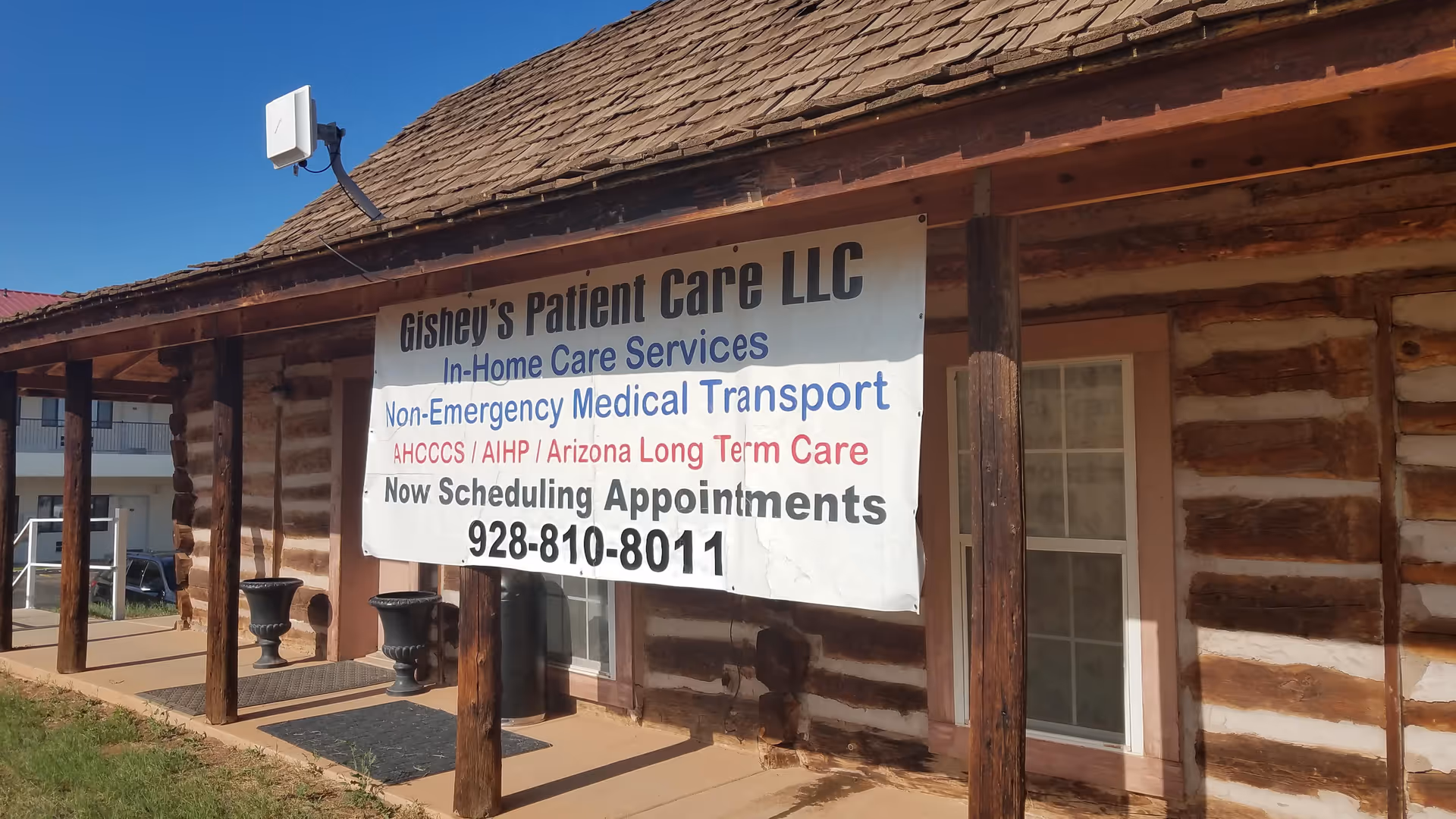 Log cabin-style building exterior with a large banner for Gishey's Patient Care LLC.