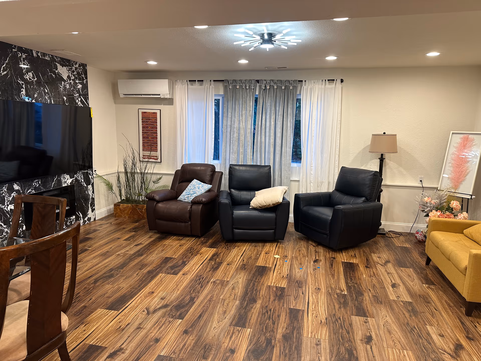 Spacious living room with three armchairs, a TV, plants, and sheer curtains.