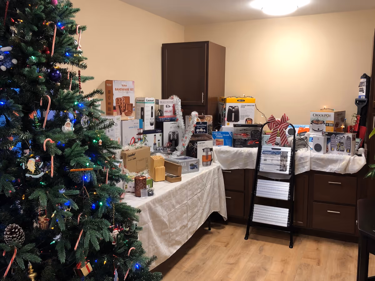 Christmas tree beside tables piled with boxed appliances in a kitchen-like interior.