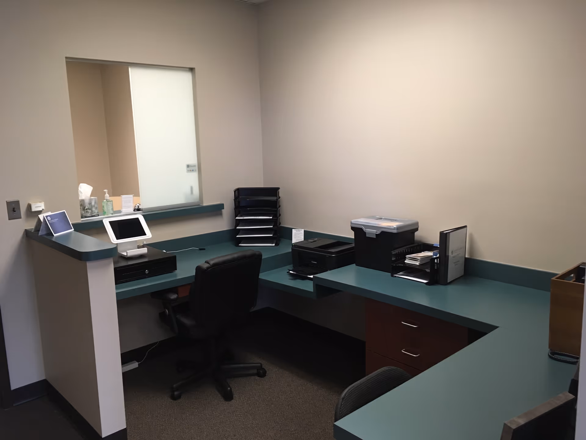 Office desk with computer, printers, and file organizers along an L-shaped green counter.
