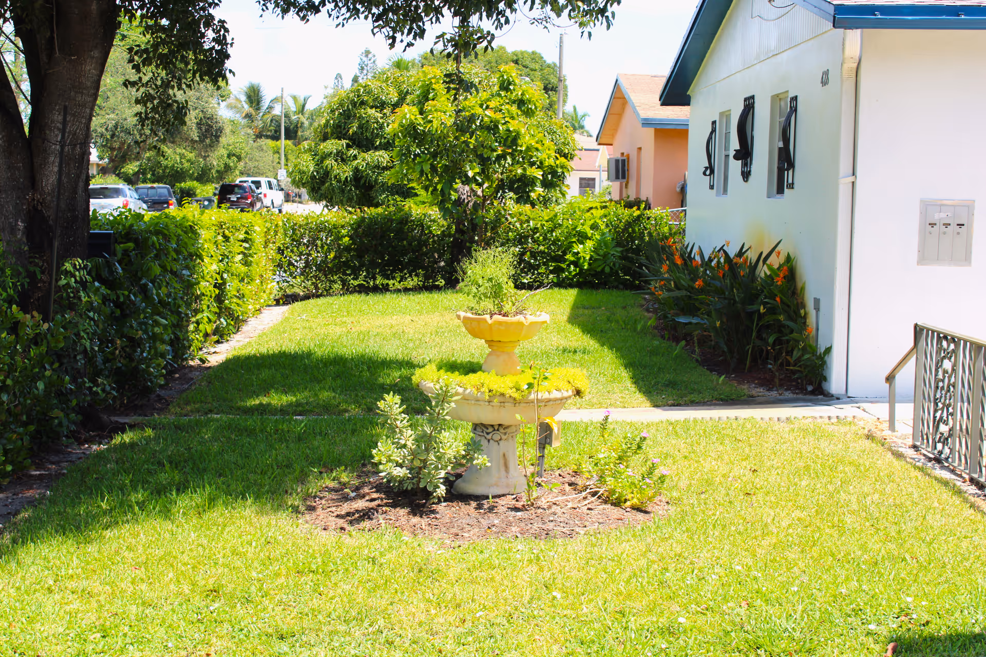 Well-maintained lawn with a three-tier fountain, shrubs, and a white building exterior.