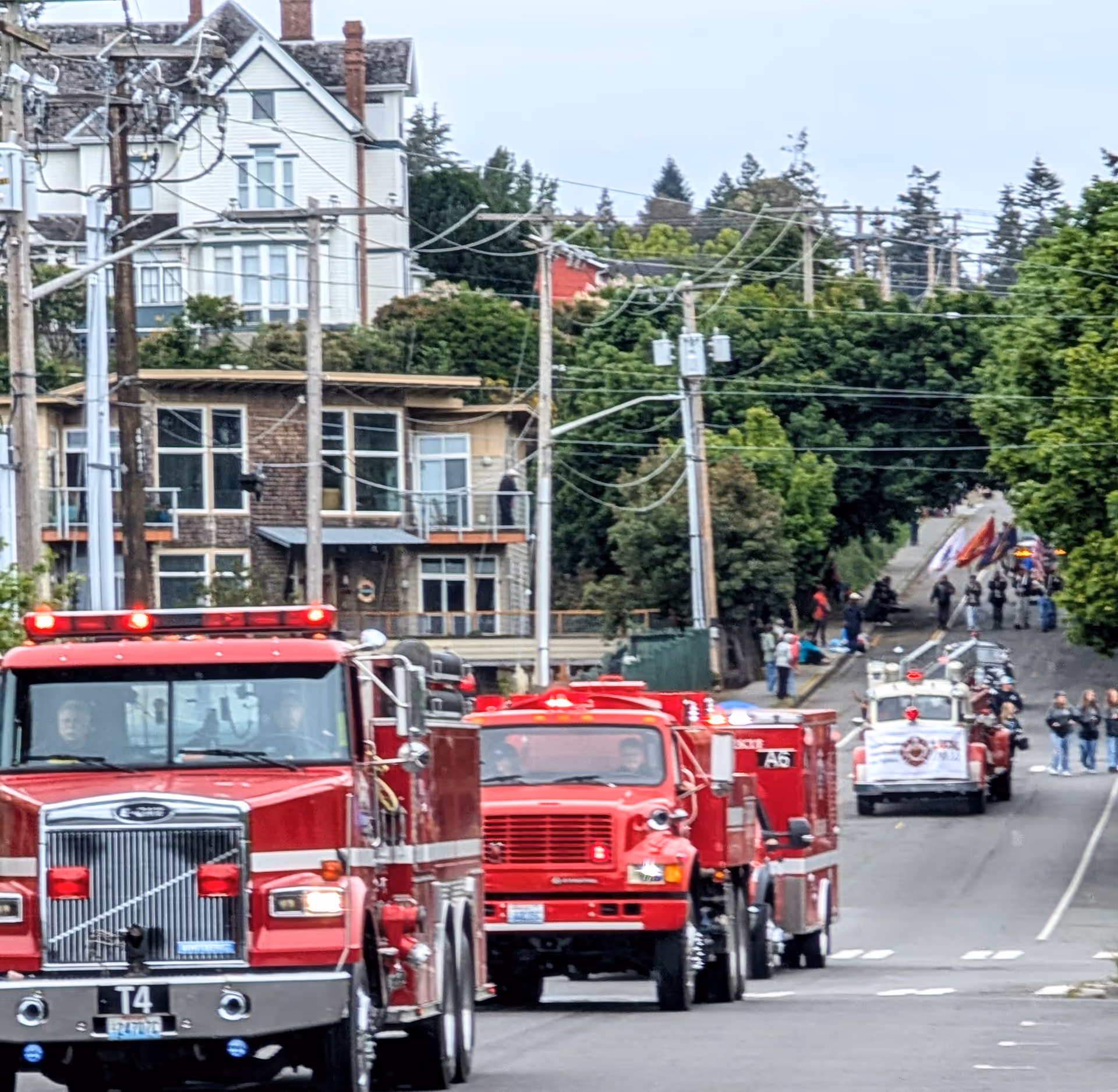 Line of red fire trucks on a city street during a parade with spectators.