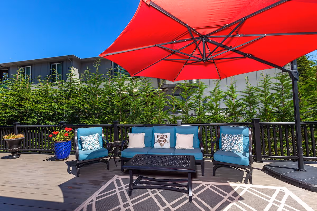 Outdoor deck patio with teal cushioned seating, a black coffee table, potted plants and a large red umbrella.