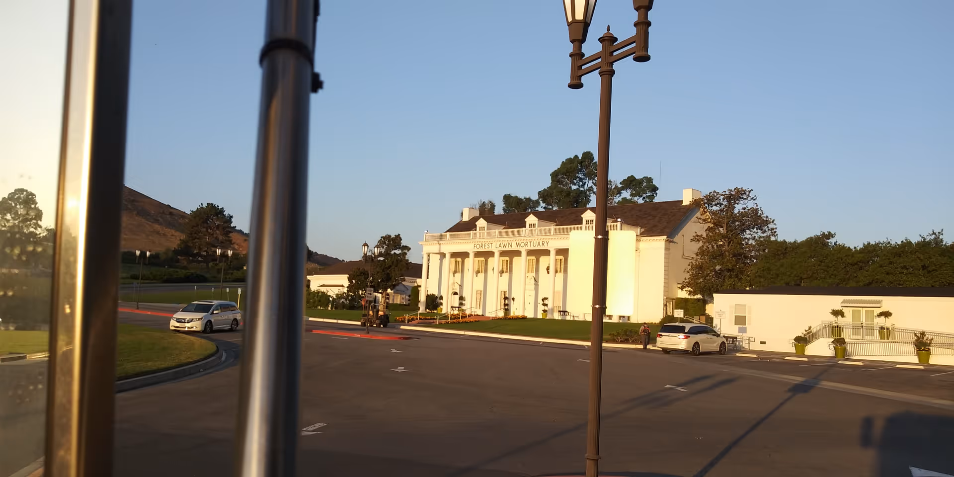 A white, columned senior living facility exterior with a curved road and parked cars.