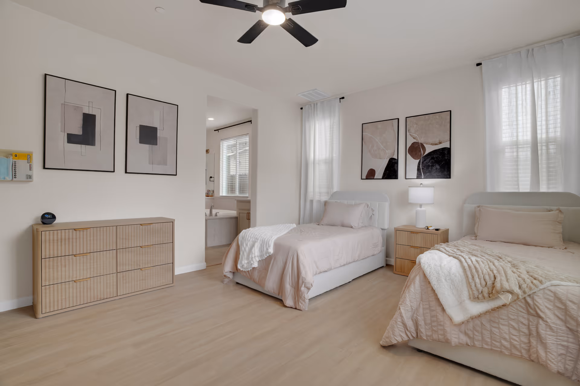 Bright, neutral twin-bedroom with two beds, dresser, nightstands, and abstract wall art.