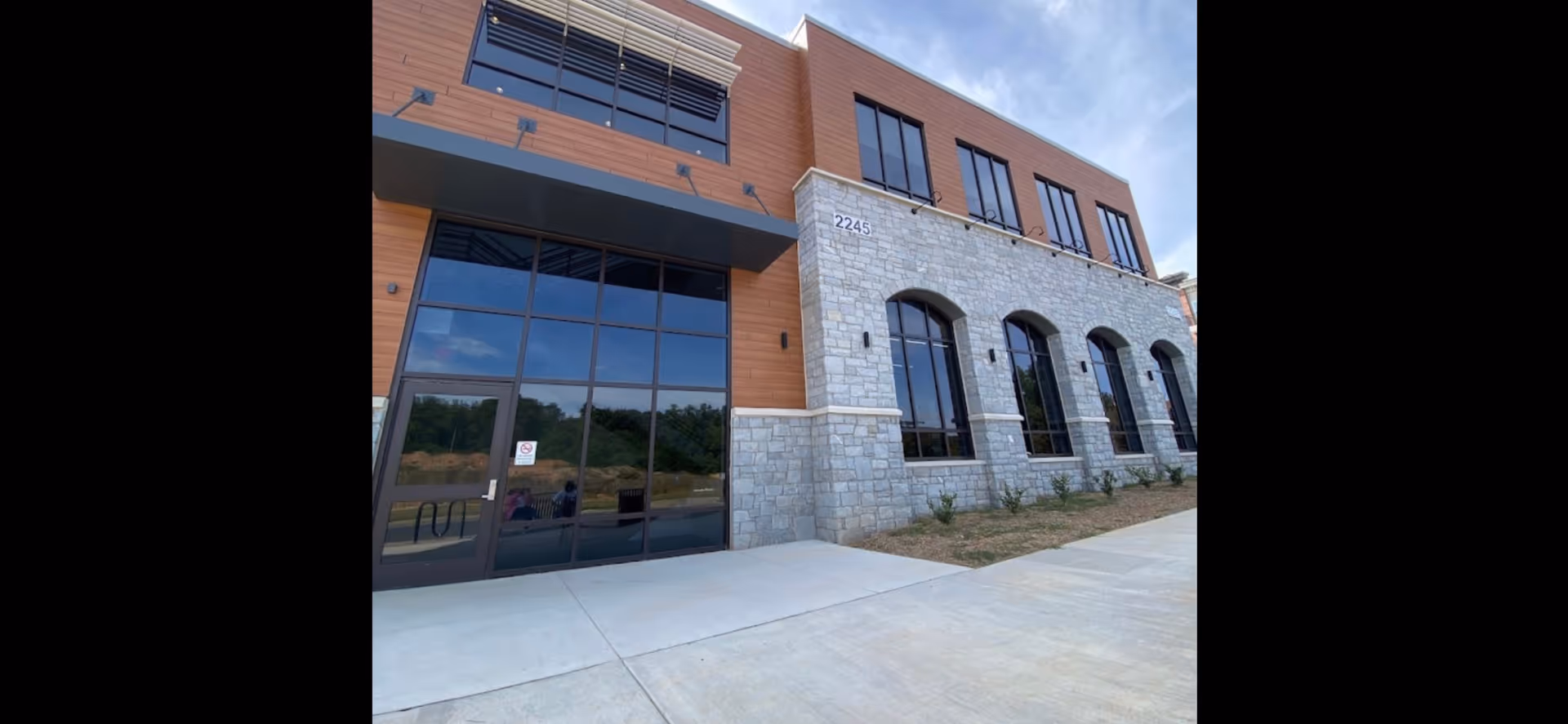 Front exterior of a modern two-story senior care building with stone, wood, and glass entrance.