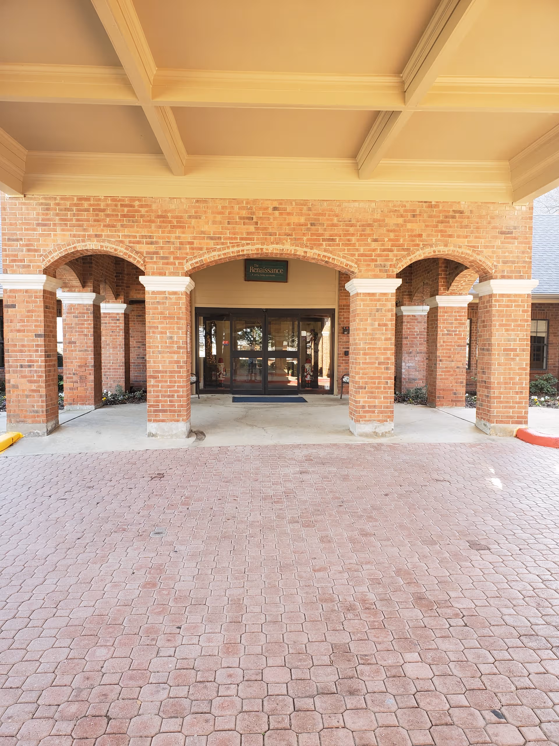 Brick entrance with arches under a beige covered porte-cochère and glass doors.