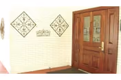 Wooden front door with glass panes on a light brick wall, decorative metal squares nearby.