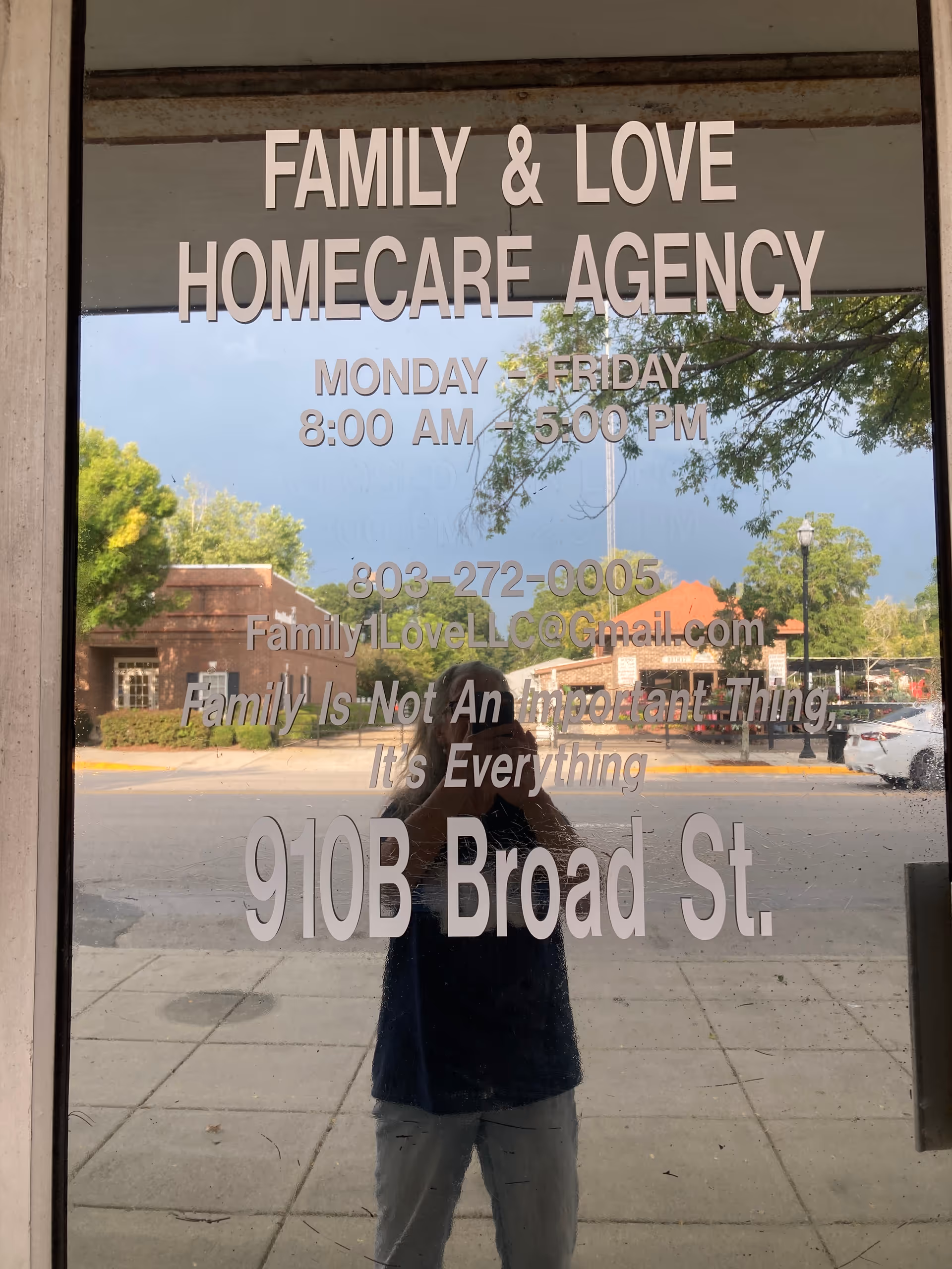 Reflection of a person taking a photo on a glass door displaying agency signage.