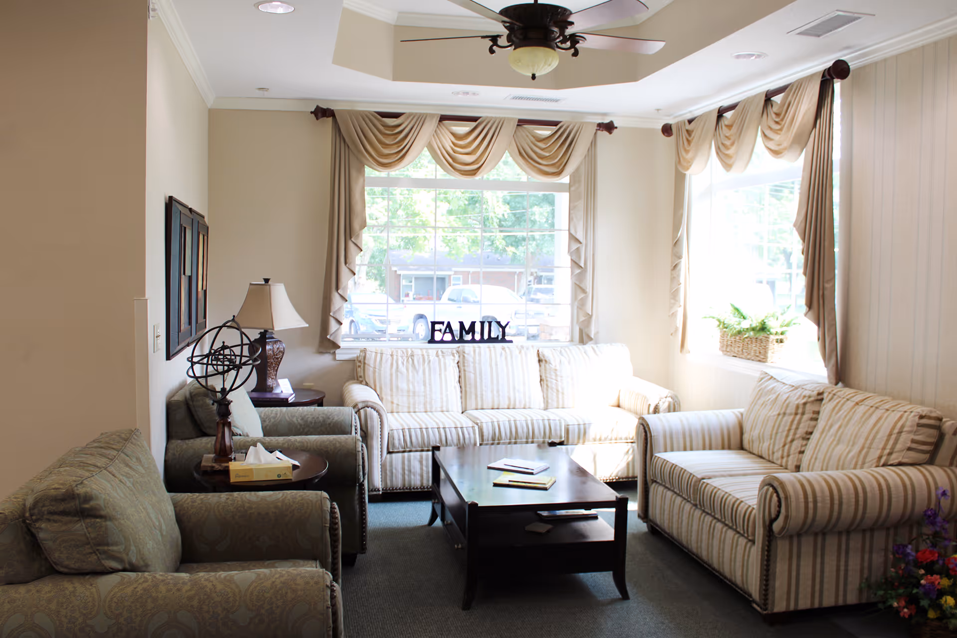 Bright living room with striped sofas, coffee table, large windows, and 'FAMILY' decor.