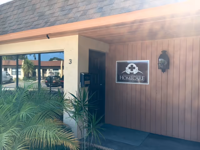 Front exterior of a home care facility entrance with sign and plants.