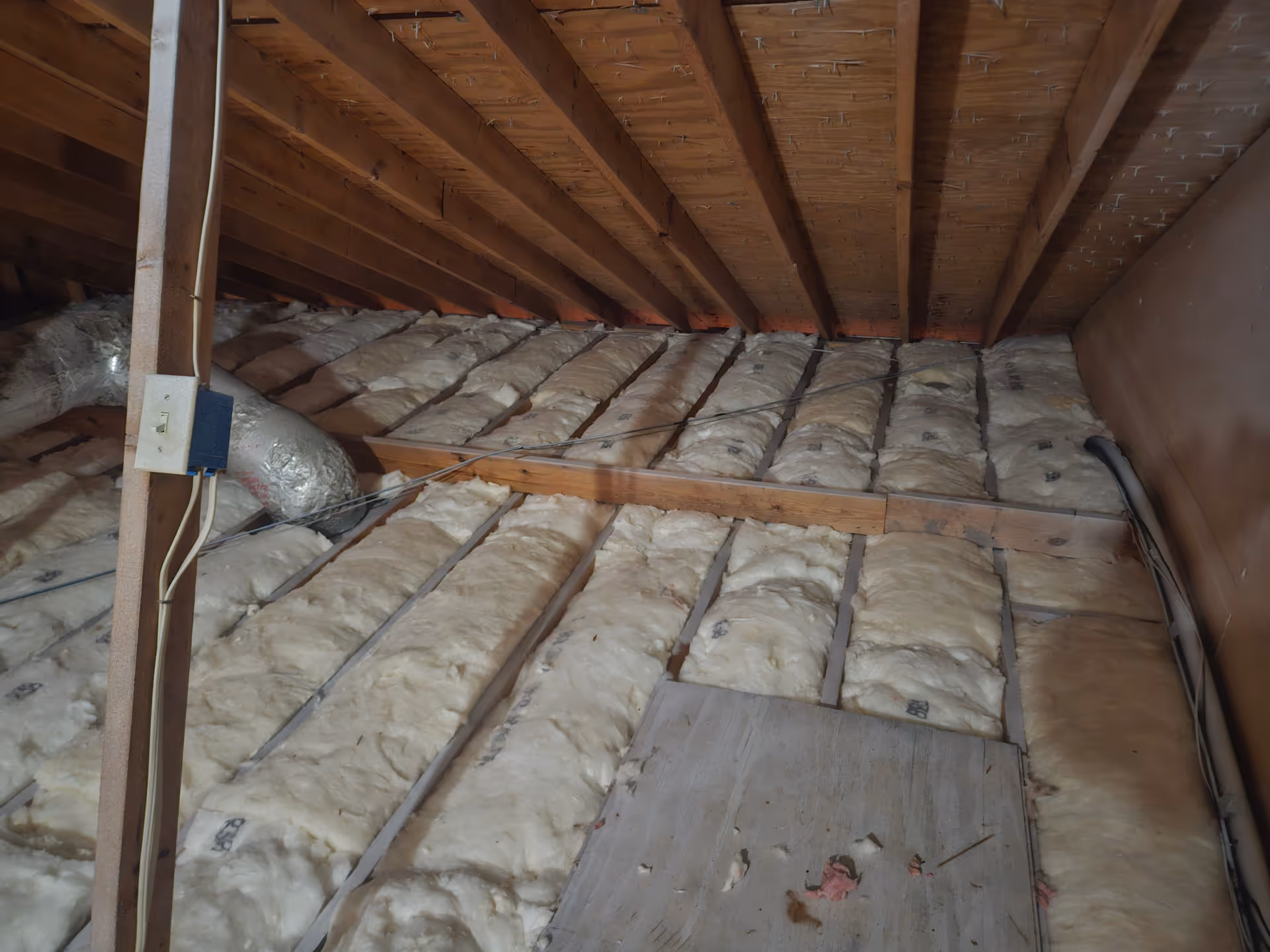 Attic space with exposed wooden joists and thick insulation across the floor.