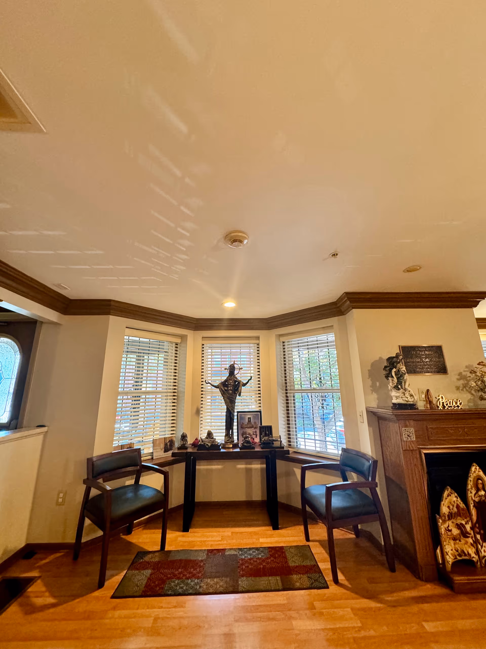 Cozy corner living area with bay windows, two chairs, a console table, a statue, and fireplace.