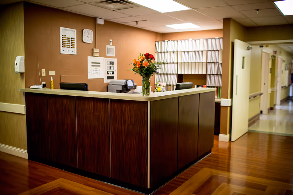 Reception desk in Lincoln Village Healthcare Center lobby with flowers and hallway beyond.