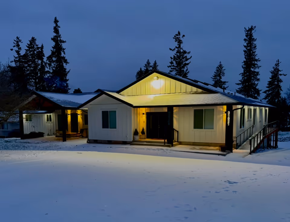 Exterior view of Daphne Adult Care Home LLC: snow-covered, illuminated entrance at dusk.