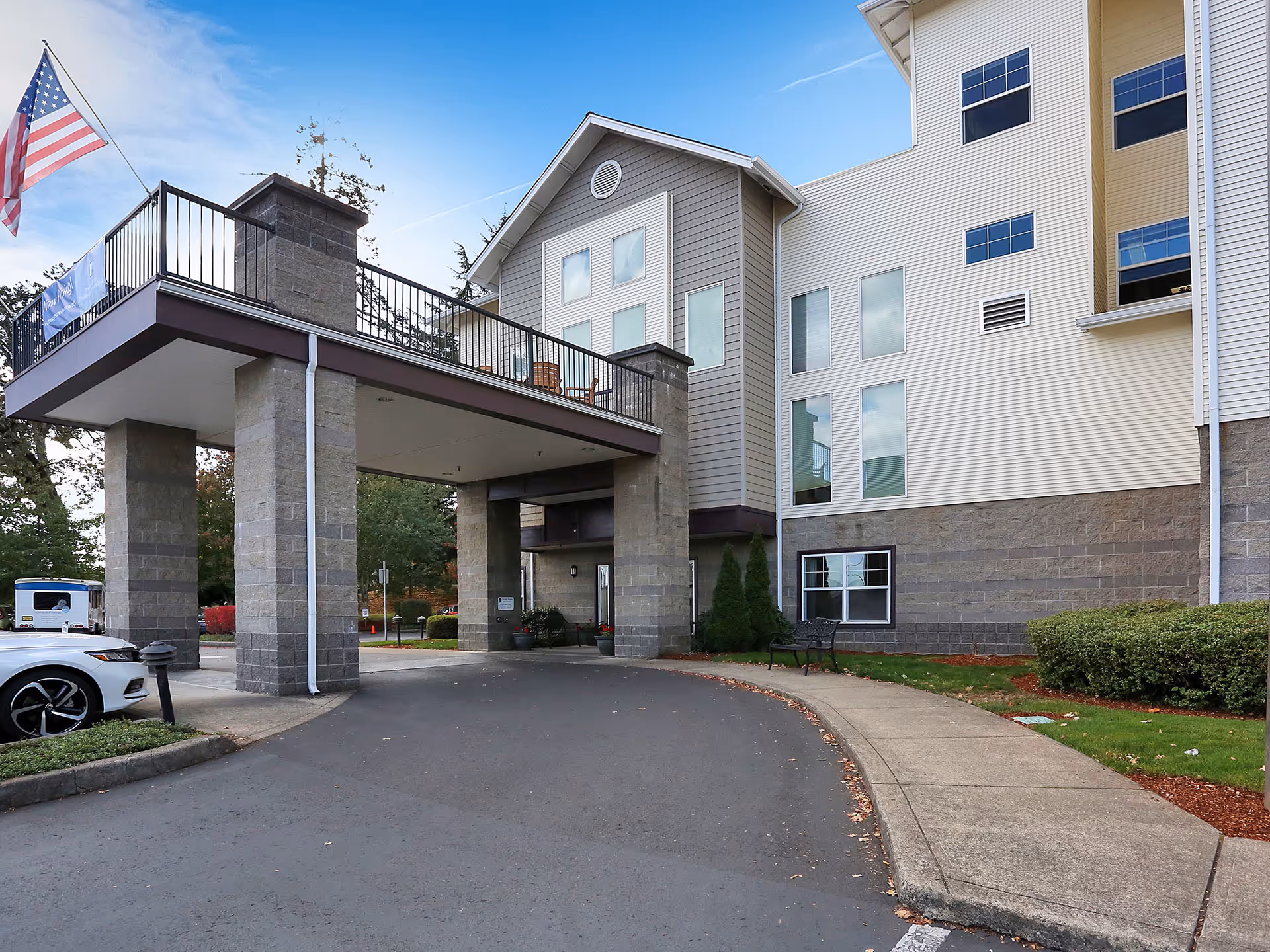 Exterior view of Prestige Senior Living Orchard Heights with entrance canopy, driveway, and flag.