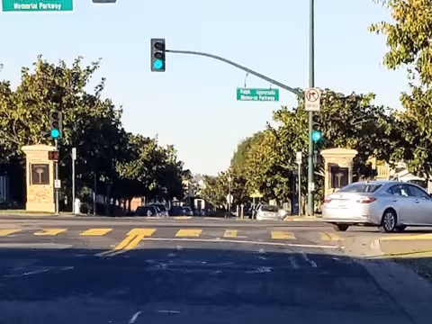 Wide street intersection with traffic lights, crosswalks, and a white car passing.